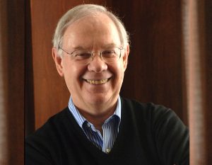 A man smiles in front of a wooden wall.