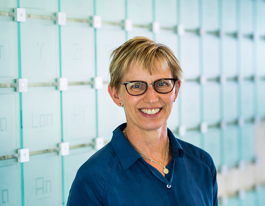 Laura Kiessling smiles in front of a glass sculpture of the periodic table of elements.