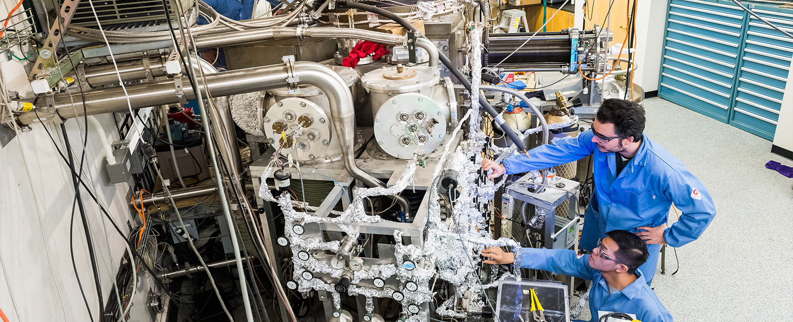 Two graduate students stand at a giant machine in a lab.