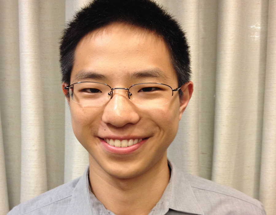 Chemistry alumnus Daniel Zhang poses in front of a cream curtain.