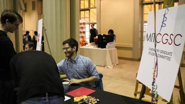 A male student sitting behind a table informs a student about an organization.