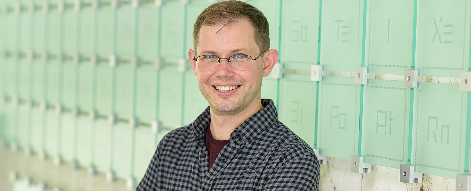 A man smiles in front of a periodic table glass sculpture.