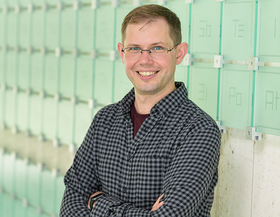 A man smiles in front of a glass periodic table of elements sculpture.