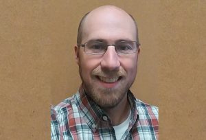 A man smiles in front of a wall.