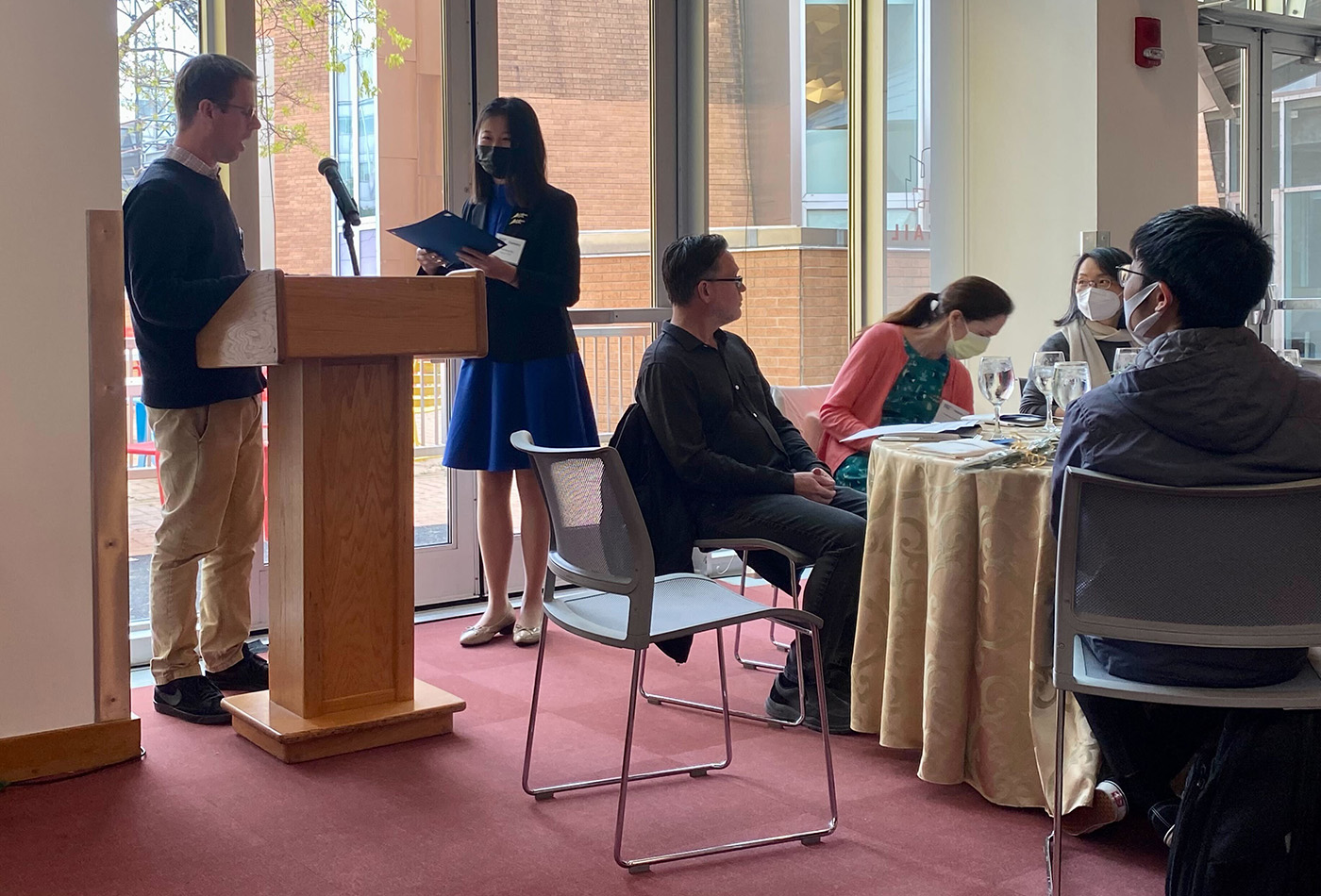 A woman in a blue dress collects an award from a faculty member at a podium.