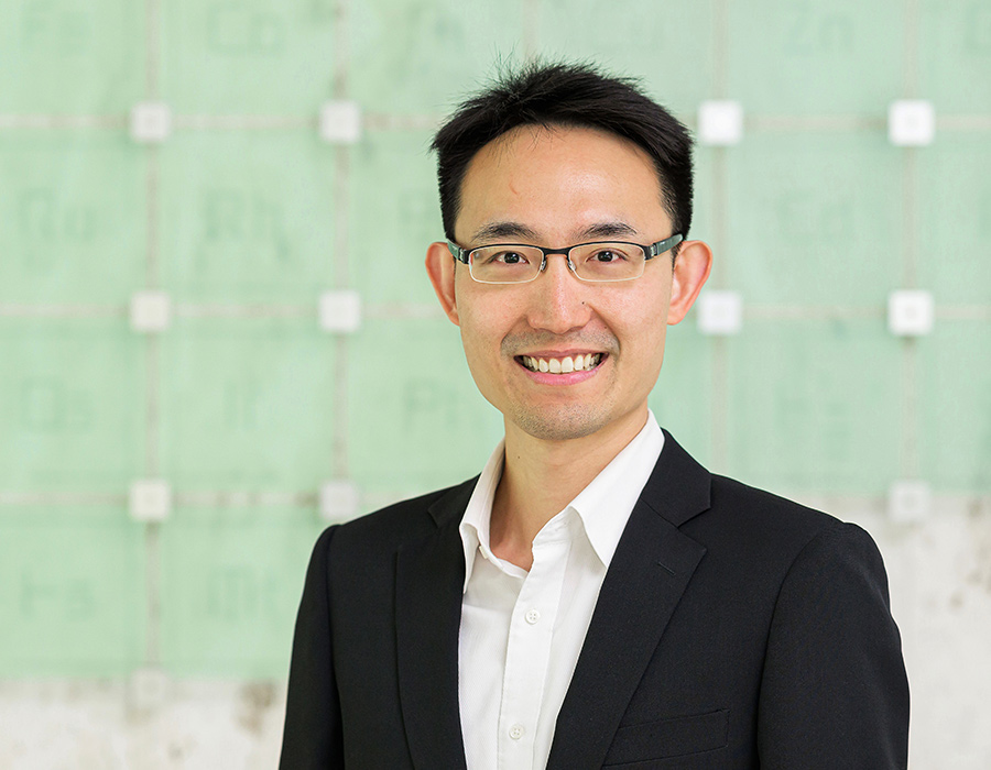 A man smiles in front of a periodic table sculpture.