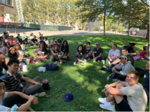 A group of graduate students sit in a circle on a green lawn.