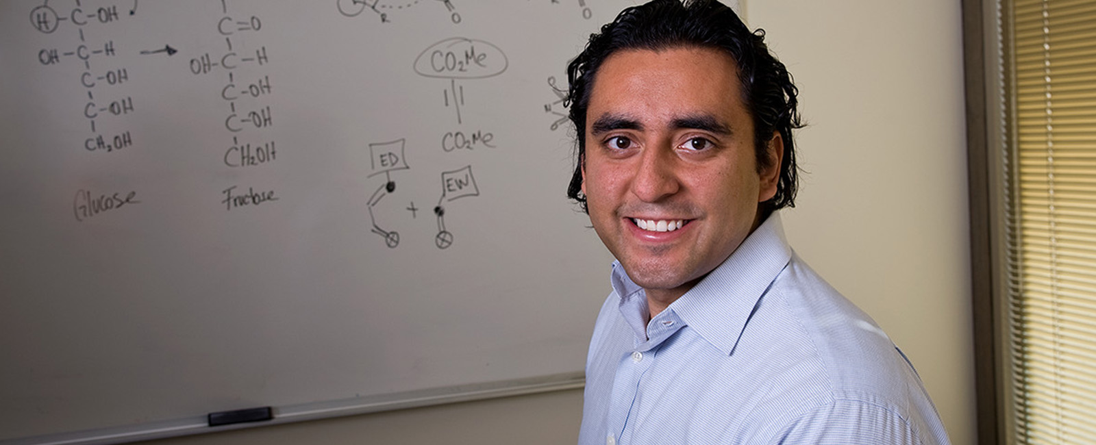 Yuriy Román smiles in front of a white board.