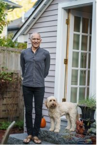 Moungi Bawendi, casually dressed, stands on the steps outside his home. His dog Phoebe poses next to him, proud of her human.