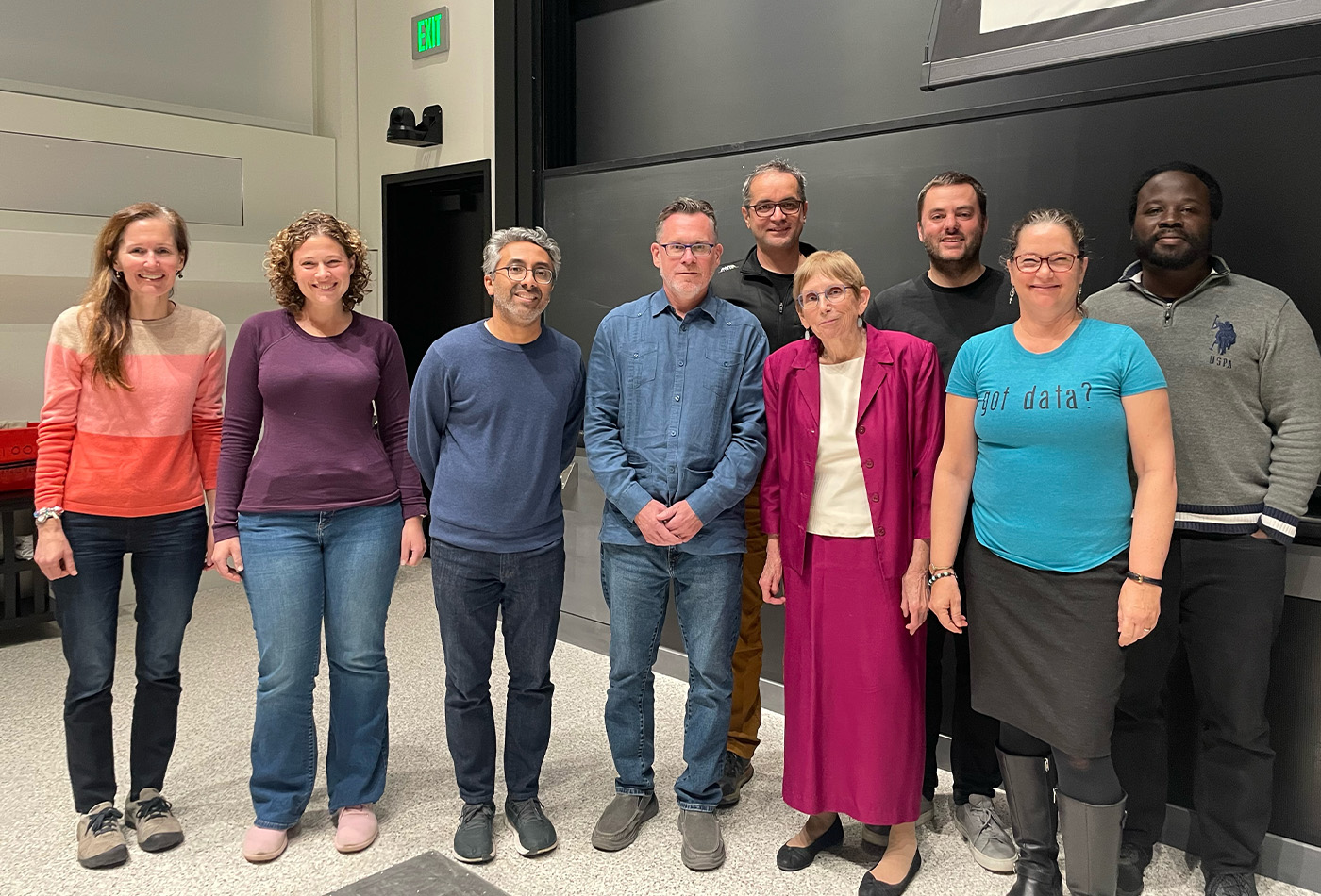 A group of faculty members smile together in a lecture hall.