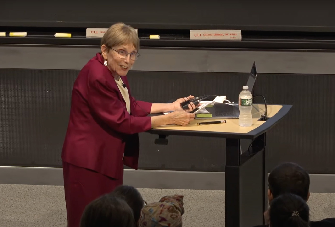 JoAnne Stubbe, wearing a dark red suit, stands at a podium.