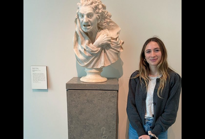 Daisy Ludlow stands smiling beside a grimacing statue.