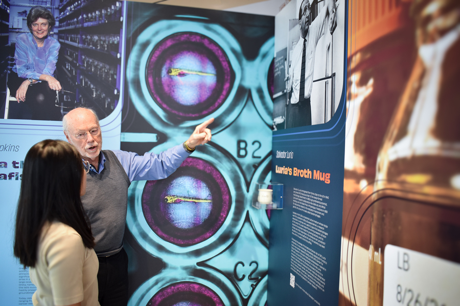 Phillip Sharp and an unidentified woman chat in front of panels of a gallery exhibit.