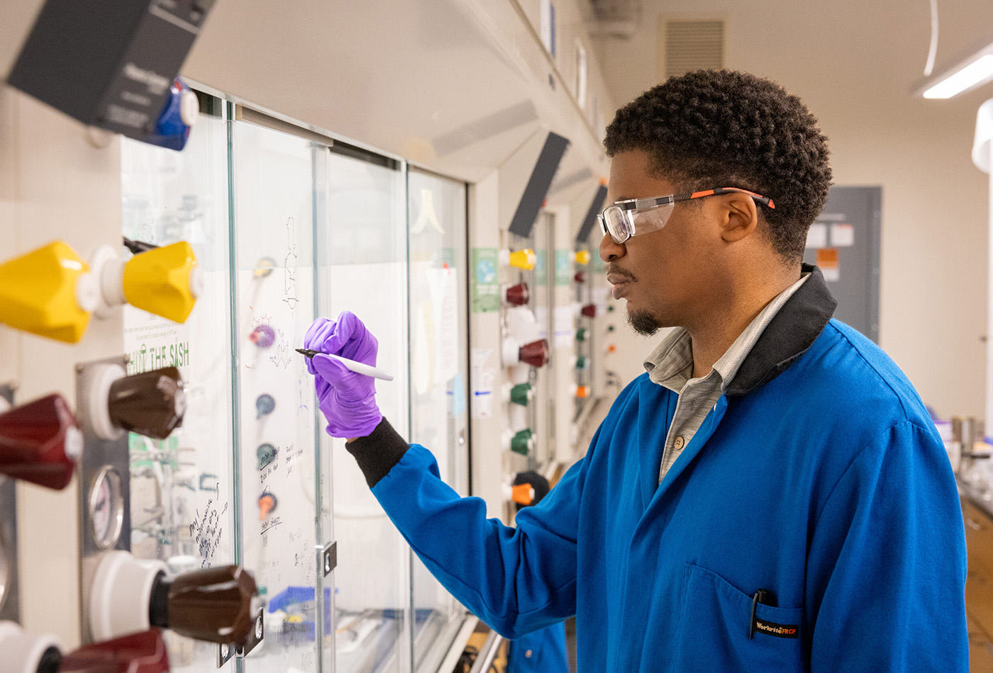 Gerard Porter, wearing a lab coat and safety glasses, conducts research at a fume hood.